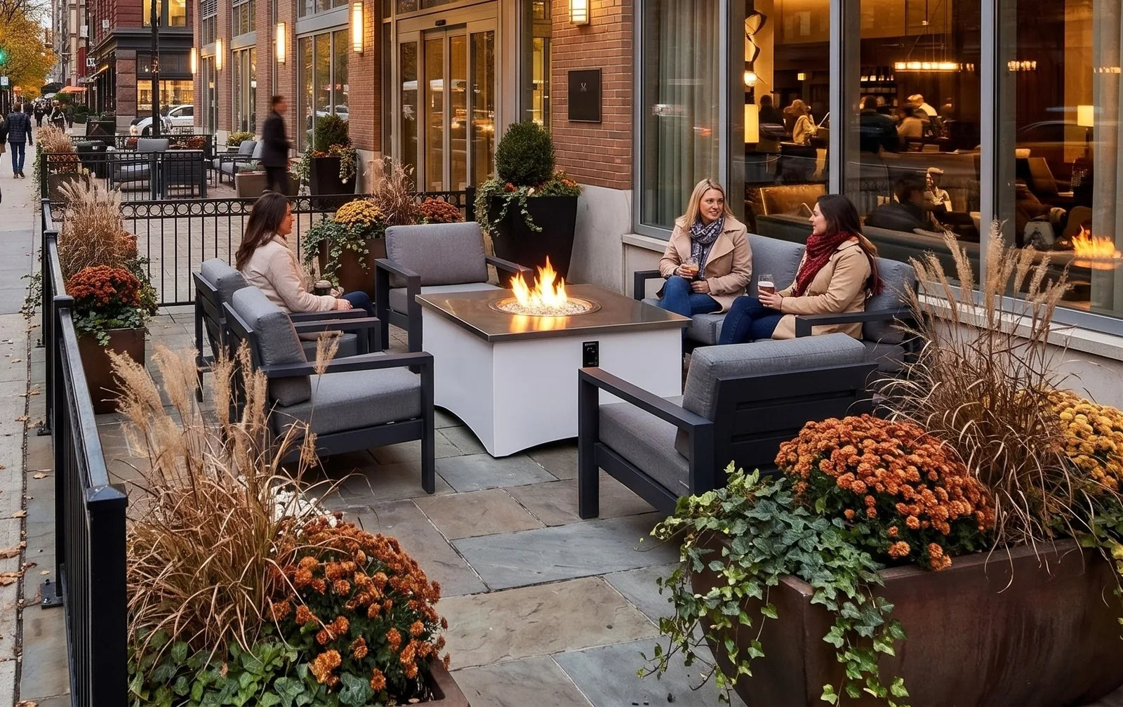 A fire table lit on a hotel terrace in autumn, with seating around it and guests in coats